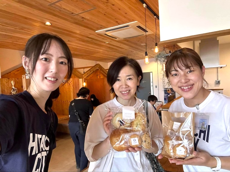 木の天井の開放的な晴耕雨読の室内。テーブル席で談笑する人たちと、壁の大型モニターやキッチン